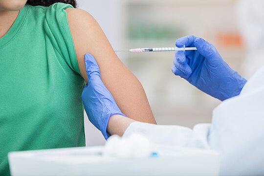 Foto: Ein Arzt verabreicht einer Person eine Impfung in den Oberarm.