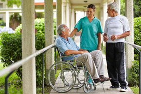 Eine Pflegerin und zwei ältere Männer unterhalten sich im Garten.