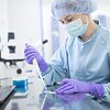 Forscherin im Labor mit Kopfbedeckung, Maske, Handschuhen und Pipette in der Hand