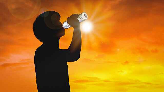 Foto: Eine Person trinkt aus einer Flasche, im Hintergrund Himmel in orange mit auf oder untergehender Sonne