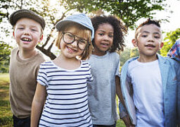 Foto: Vier Kinder unterschiedlicher Nationalität im Alter von ungefähr 10 Jahren stehen vor einem Baum und schauen in die Kamera