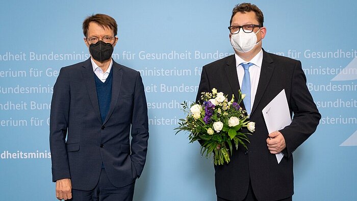Bundesgesundheitsminister Prof. Dr. Karl Lauterbach mit dem Patientenbeauftragten Stefan Schwartze (beide mit Masken), Schwartze mit Blumenstrauß und Ernennungsurkunde in den Händen