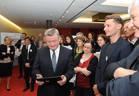 Foto: Minister Gröhe schaut auf ein Smartpad, das er in den Händen hält.