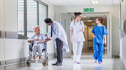 Krankenhausflur mit Ärzten, Pflegern und einer Patientin im Rollstuhl