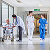 Krankenhausflur mit Ärzten, Pflegern und einer Patientin im Rollstuhl