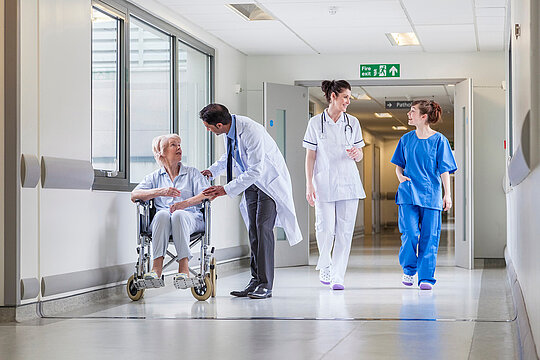 Krankenhausflur mit Ärzten, Pflegern und einer Patientin im Rollstuhl