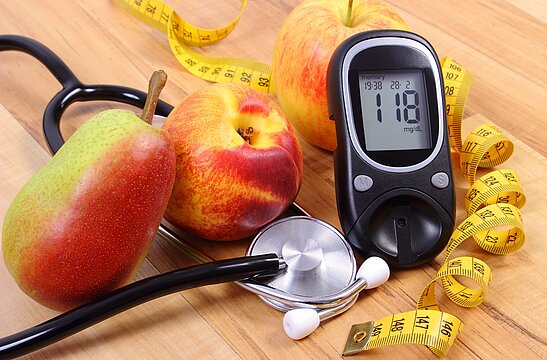 Symbolfoto: Eine Zusammenstellung mit Blutzuckermessgerät, Stethoskop, etwas Obst und einem Maßband auf einem Holztisch