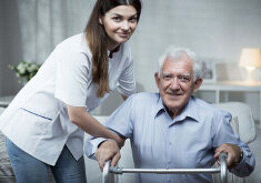 Foto: älterer Herr an Gehhilfe mit Betreuungskraft neben sich