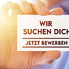 Eine Hand hält eine Karte hoch mit der Aufschrift: "Wir suchen dich - jetzt bewerben"