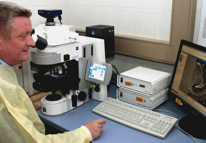 Foto: Minister Gröhe sitzt an einem Labortisch vor einem Mikroskop und schaut auf einen Monitor, der die Probe im Objektträger unter dem Mikroskop anzeigt (Bildquelle: BMG/Krampe)
