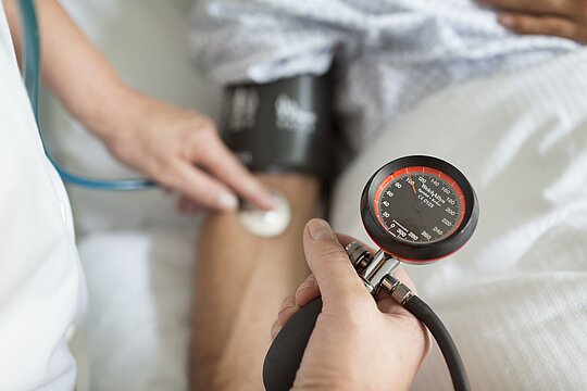 Foto: Arzt mit Blutdruck- und Pulsmessgerät am Arm eines Patienten.