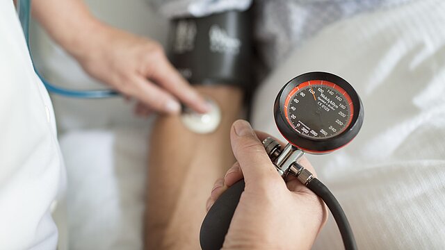 Foto: Arzt mit Blutdruck- und Pulsmessgerät am Arm eines Patienten.