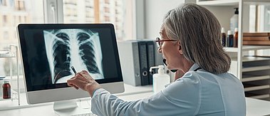 Frau schaut auf ein Röntgenbild auf einem Monitor