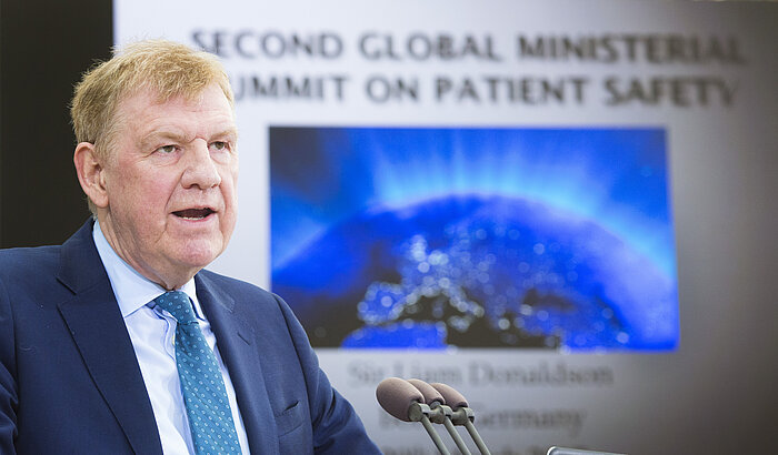 Foto: Sir Liam Donaldson spricht in Richtung des Betrachters an seinem Rednerpult, im Hintergrund ist eine Präsentationsfolie mit einer Weltkugel und der Überschrift "Second Global Ministerial Summit on Patient Safety" zu sehen