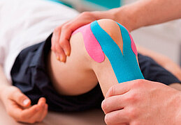 Ein Physiotherapeut führt bei einem Kind eine Knie-Übung durch. Um das Knie sind zwei Pflaster geklebt.