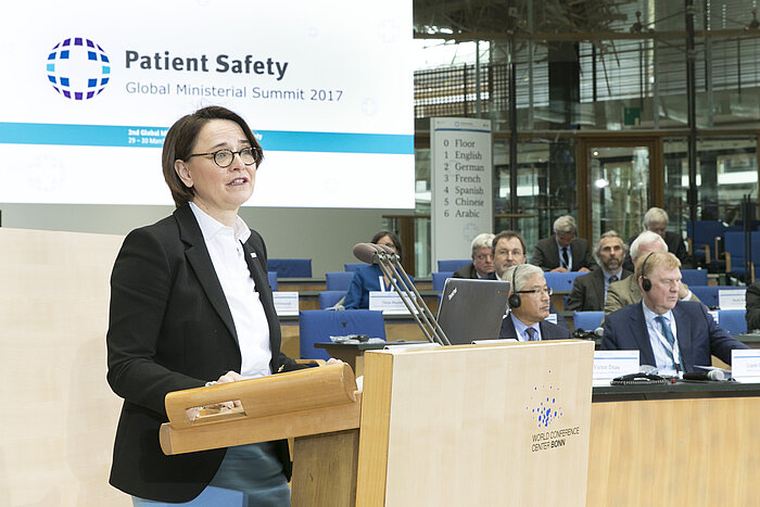 Foto: Annette Widmann-Mauz vor dem Rednerpult, im Hintergrund das Patient Safety Summit Logo