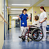 Ärztin erklärt im Krankenhausflur etwas einer älteren Patientin, die im Rollstuhl sitzt