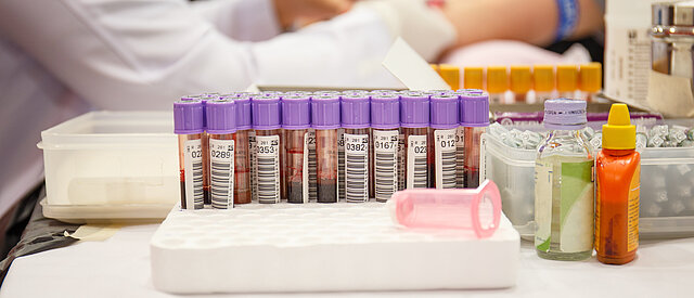 Labor mit Krankenschwester, die dem Patienten eine Blutprobe entnimmt, im Hintergrund Blutproben 
