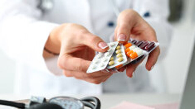 Foto: Eine Frau in weißem Kittel hält eine Auswahl an unterschiedlichen Tabletten in Blister-Verpackungen in der Hand 