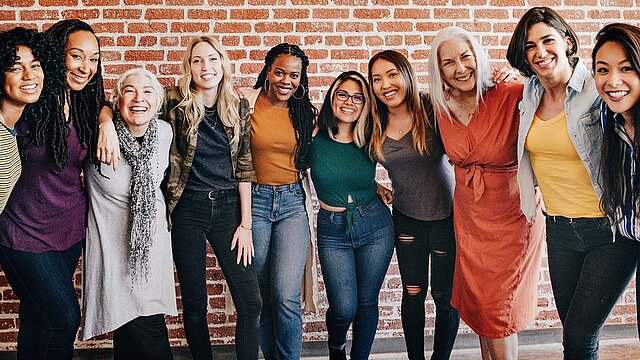 Eine Gruppe Frauen stehen Arm in Arm in die Kamera schauend nebeneinander