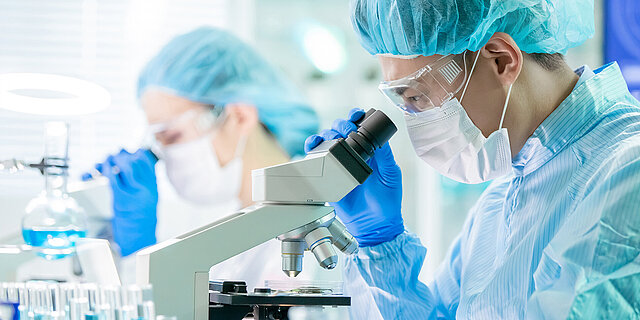 Personal in einem Labor schaut durch Mikroskope.