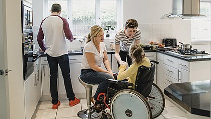Eine Familie pflegt ihre im Rollstuhl sitzende Tochter zuhause in der Küche.