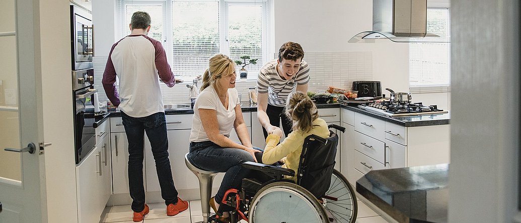 Eine Familie pflegt ihre im Rollstuhl sitzende Tochter zuhause in der Küche.