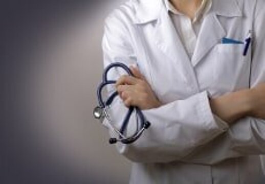 Foto: vor einem dunklen Hintergrund steht ein Arzt in weißem Kittel (nur der Oberkörper ist zu sehen) mit blauem Stethoskop und verschränkten Armen