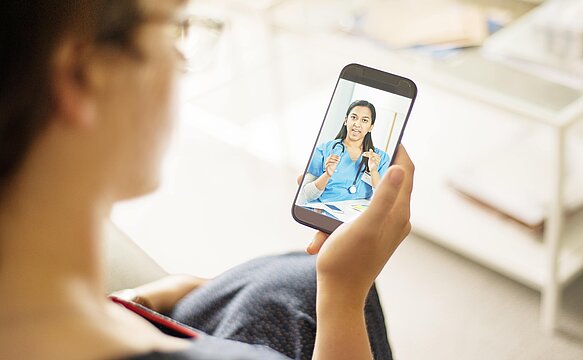 Foto: Eine Patientin schaut in ihr Handy, in dem eine Ärztin spricht