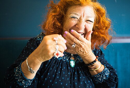 Eine ältere Dame lacht herzlich und hält sich die Hand vor den Mund.