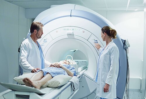 Ein Patient liegt in einem CT Gerät und daneben steht medizinisches Personal