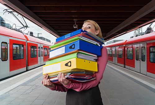 EIne Frau trägt einen Stapel AKten über einen Bahnhof